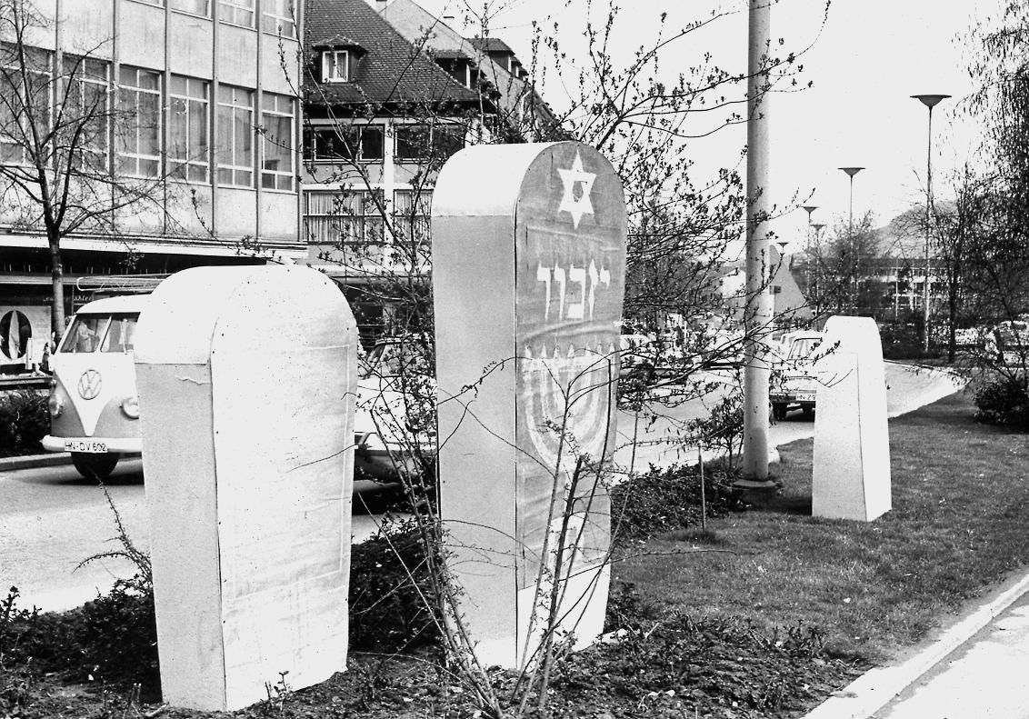 Eine Gedenktafel, ein Obelisk oder ein Gedenkstein für die in der Progromnacht 1938 abgebrannte Synagoge? 1965 stellt die Stadt Attrappen auf dem Mittelstreifen der Allee auf, um endlich zu einer Entscheidung zu kommen.