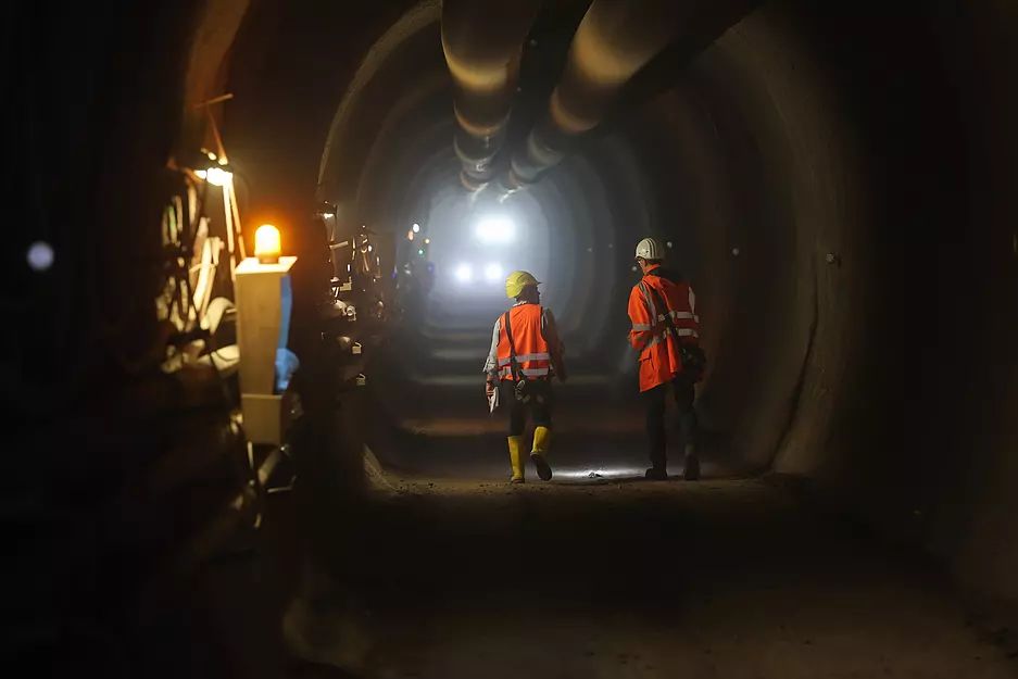 Durch den Fluchtstollen gehen Arbeiter. An der Wand leuchtet ein Warnlicht.